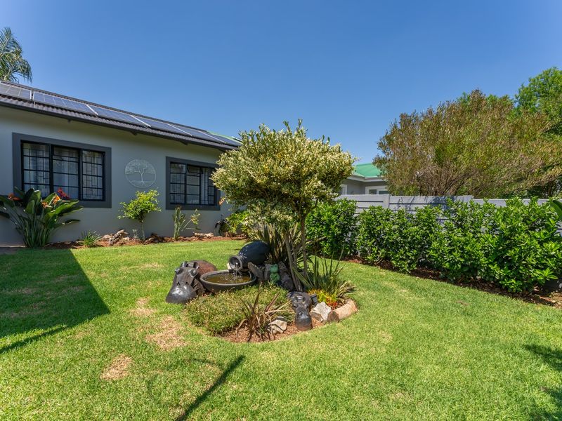 A well-maintained rear garden featuring a landscaped lawn, established shrubbery, a decorative water feature, and solar panels installed on the roof.