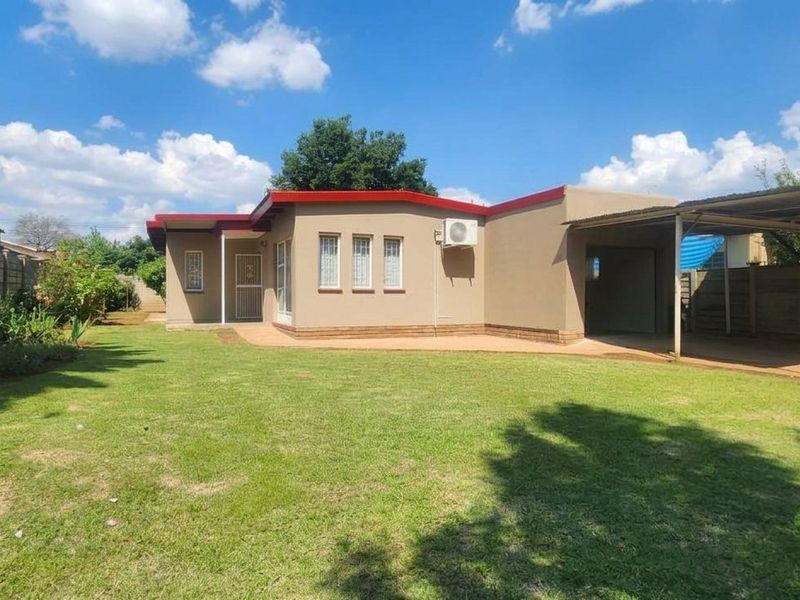 Rear view of the house featuring a spacious lawn, a paved patio area, and an attached carport structure.