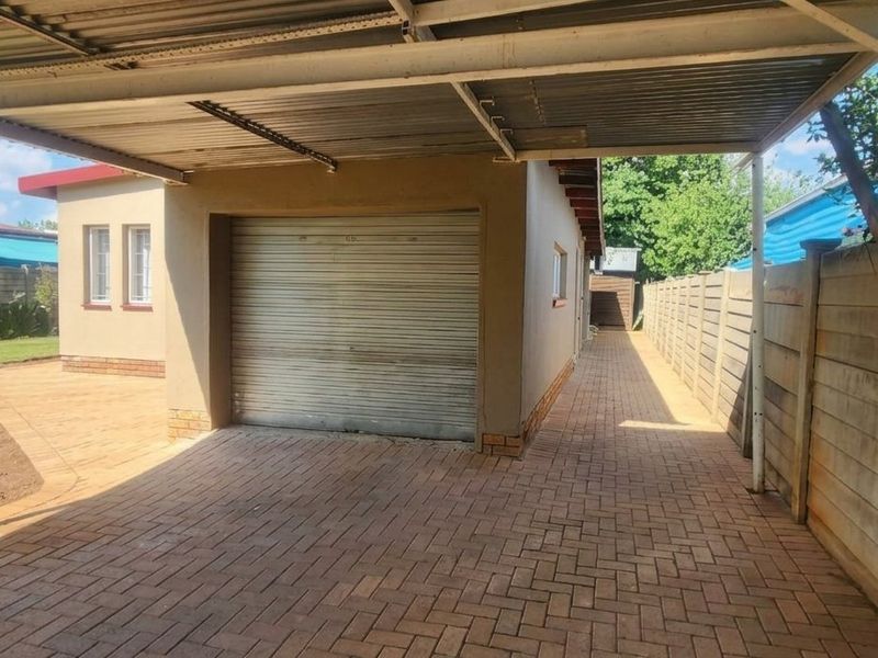 A detached garage featuring a roller shutter door, covered by a metal carport structure, set within a paved yard with precast boundary walls.