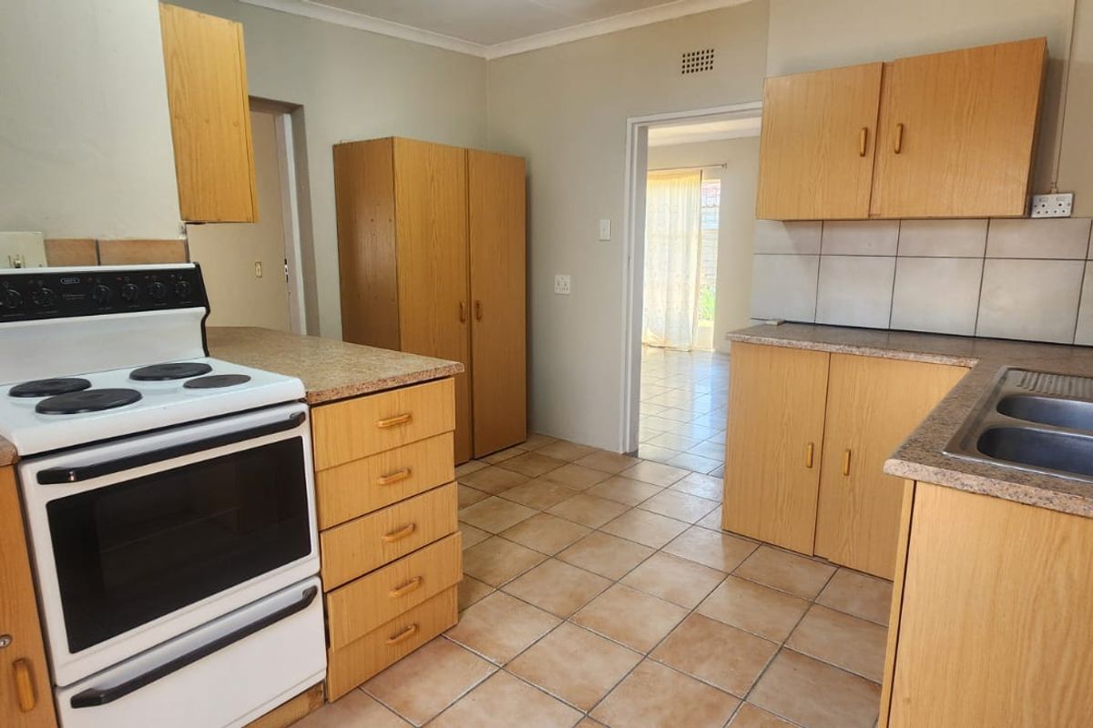 A dated kitchen featuring laminate cabinetry, a double bowl stainless steel sink, and a freestanding electric stove with ceramic tiled flooring.