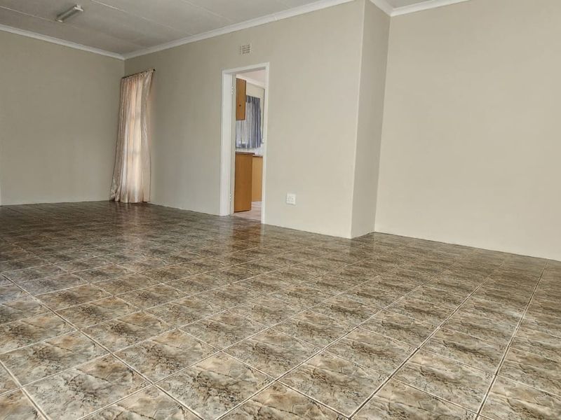 A spacious, empty living area featuring neutral walls and tiled flooring, providing a blank canvas for interior design.