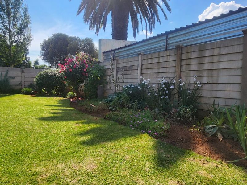 A well-maintained private garden featuring a lush green lawn, established garden beds, and a secure precast concrete boundary wall.