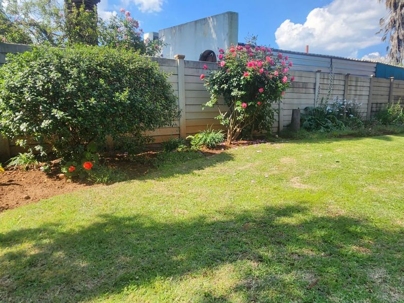 A well-maintained residential garden featuring a manicured lawn, established garden beds, and a secure precast concrete boundary wall.