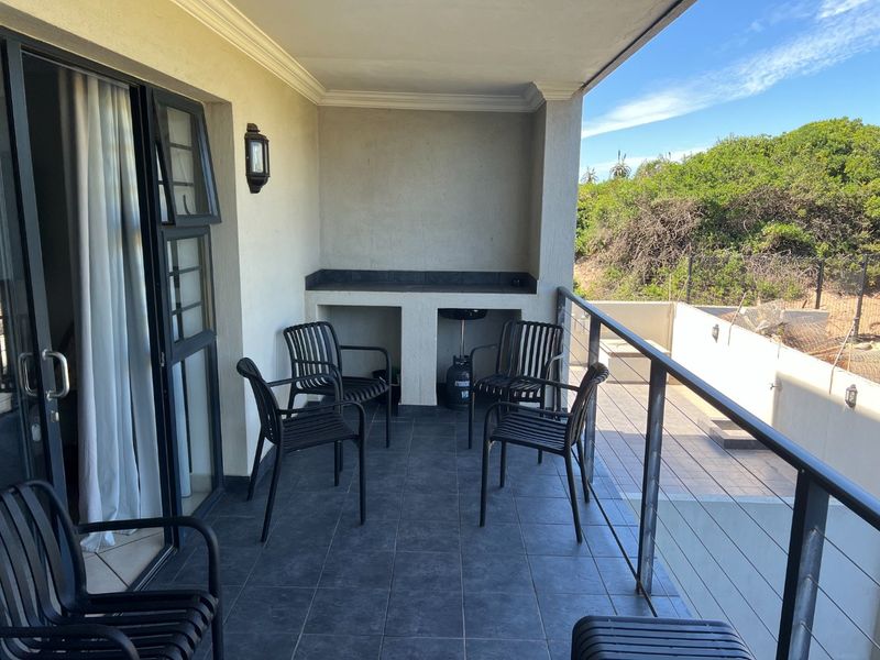 A covered balcony featuring tiled flooring, a built-in braai area, and metal railings, offering an outdoor space suitable for relaxation and entertaining.