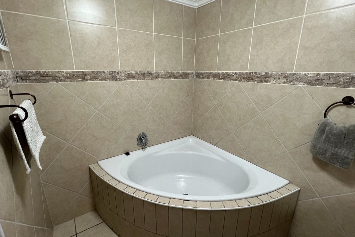A clean bathroom featuring a built-in corner bathtub with neutral-toned wall and floor tiling and a decorative mosaic tile accent border.