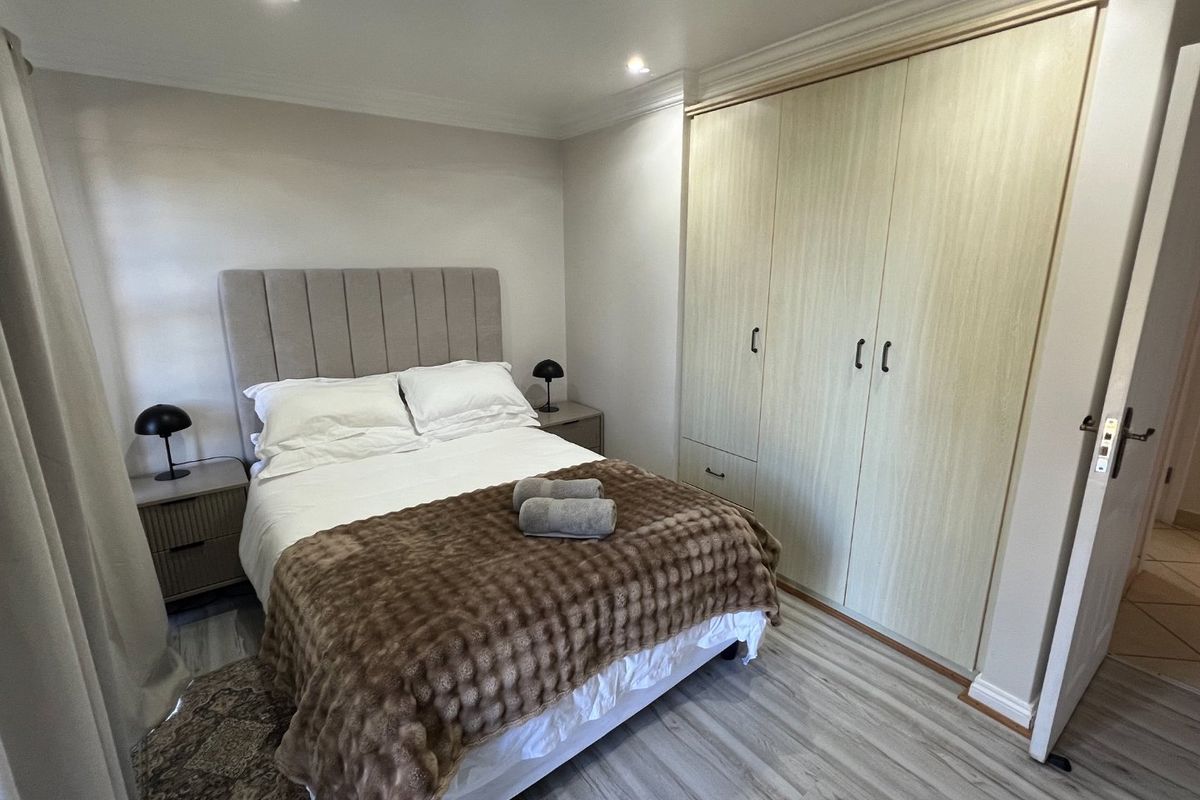 A well-maintained bedroom featuring light-toned laminate flooring, recessed ceiling lighting, and ample built-in cupboard storage.