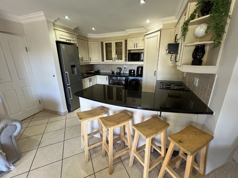 A functional kitchen featuring built-in cabinetry, granite countertops, an integrated hob, and a breakfast bar, finished with tiled flooring and decorative cornicing.