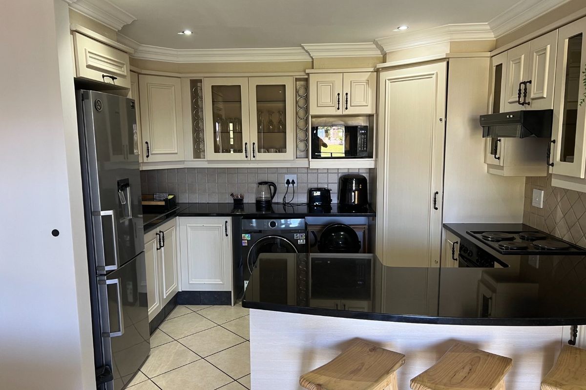 A well-maintained kitchen featuring cream cabinetry, black granite countertops, tiled backsplash, and integrated appliances, including a breakfast bar area.