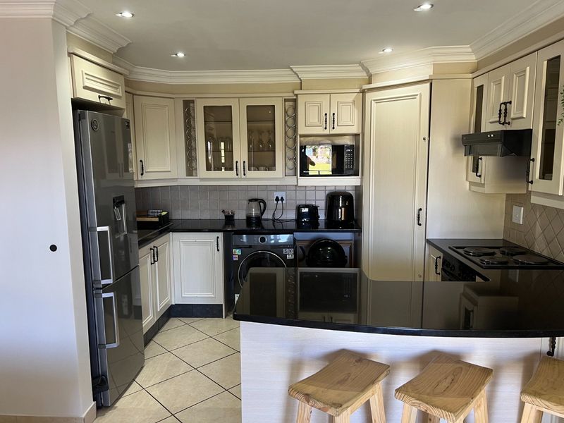 A well-maintained kitchen featuring cream cabinetry, black granite countertops, tiled backsplash, and integrated appliances, including a breakfast bar area.