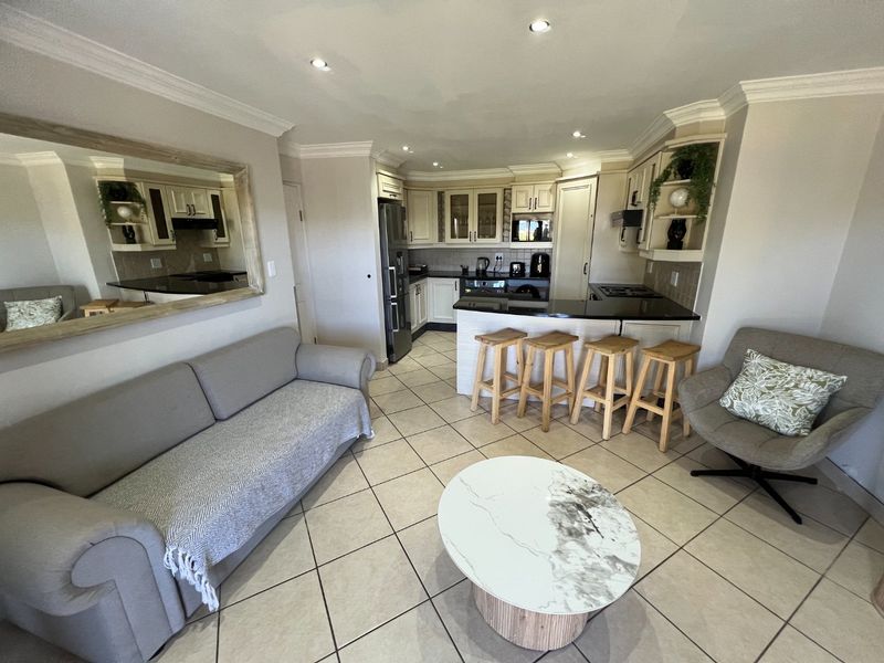An open-plan living and kitchen area featuring tiled flooring, recessed lighting, and a functional kitchen with built-in cabinetry and a breakfast bar.