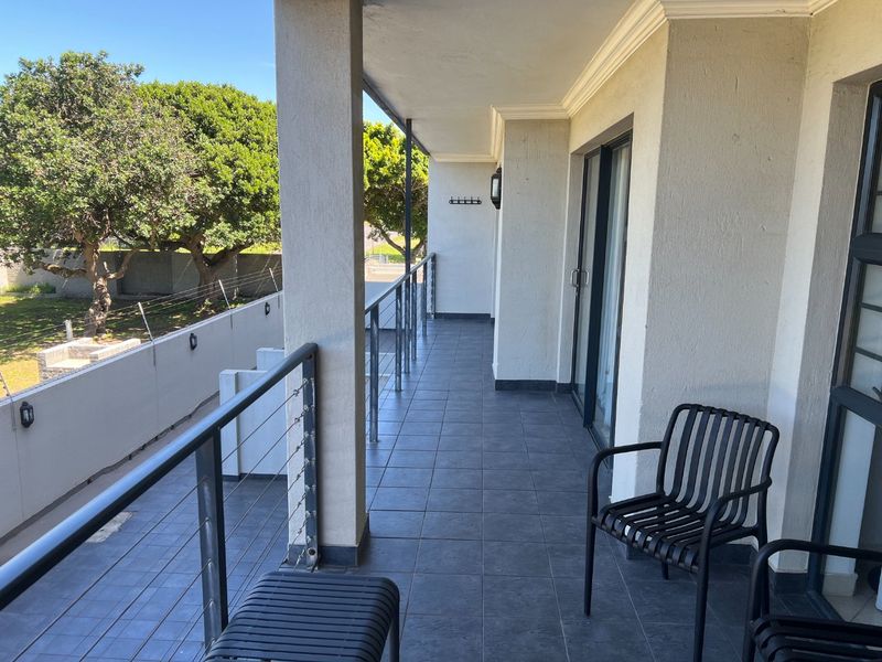 A spacious covered balcony featuring dark tiled flooring, stainless steel cable railings, and sliding glass door access to the apartment interior.