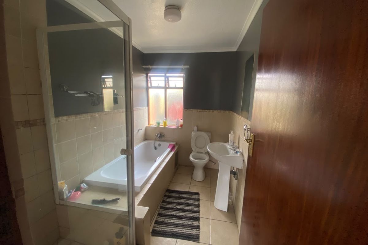 A functional bathroom featuring a bathtub with a glass screen, a pedestal basin, and a toilet, finished with neutral wall and floor tiles.