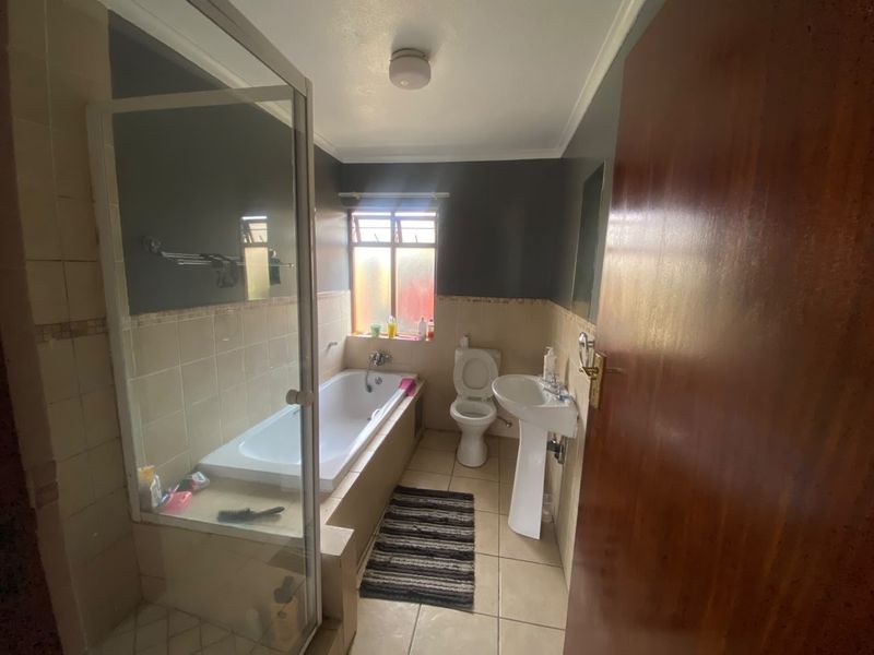 A functional bathroom featuring a bathtub with a glass screen, a pedestal basin, and a toilet, finished with neutral wall and floor tiles.