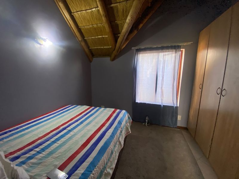 A bedroom featuring a unique exposed thatch ceiling with timber rafters and built-in wooden cupboards.