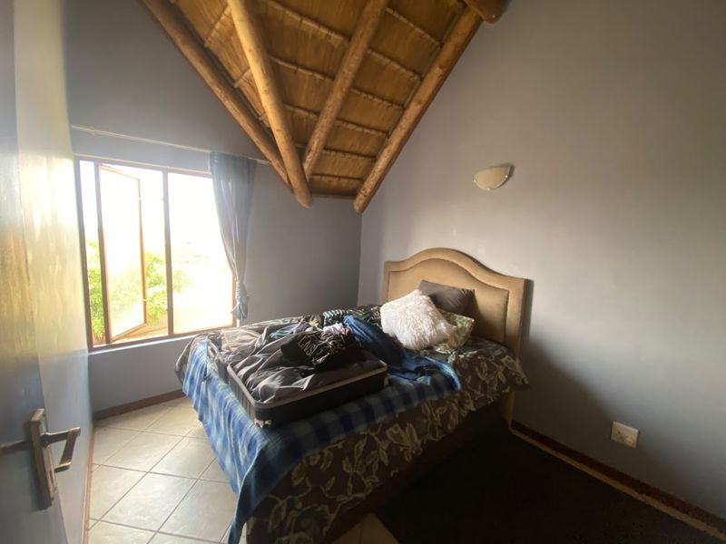 A bedroom featuring a high vaulted ceiling with exposed timber rafters and thatch, tiled flooring, and a window providing natural light.