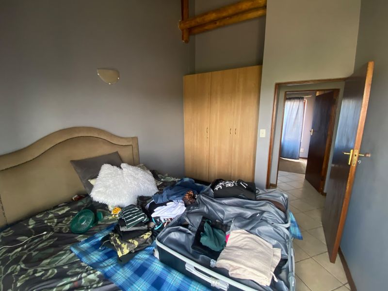A bedroom featuring built-in cupboards, tiled flooring, and an exposed timber ceiling beam, with access to an adjoining room.