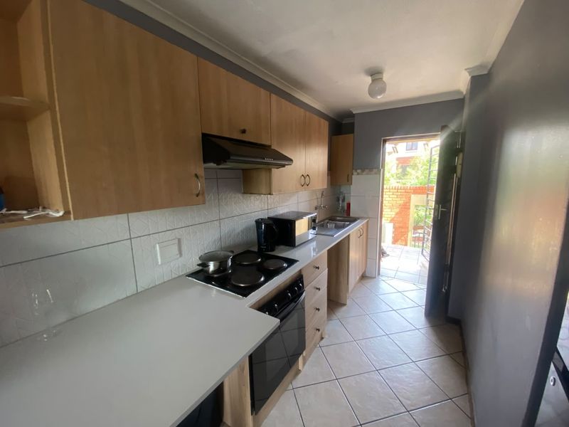 A functional galley-style kitchen featuring built-in cabinetry, an electric hob, oven, extractor fan, and direct access to an outdoor area.