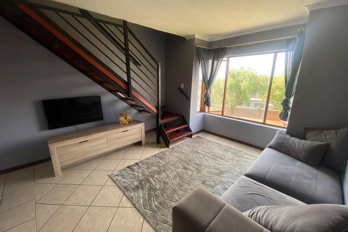 A living room featuring tiled flooring, a large window providing natural light, and an internal staircase with a metal balustrade.