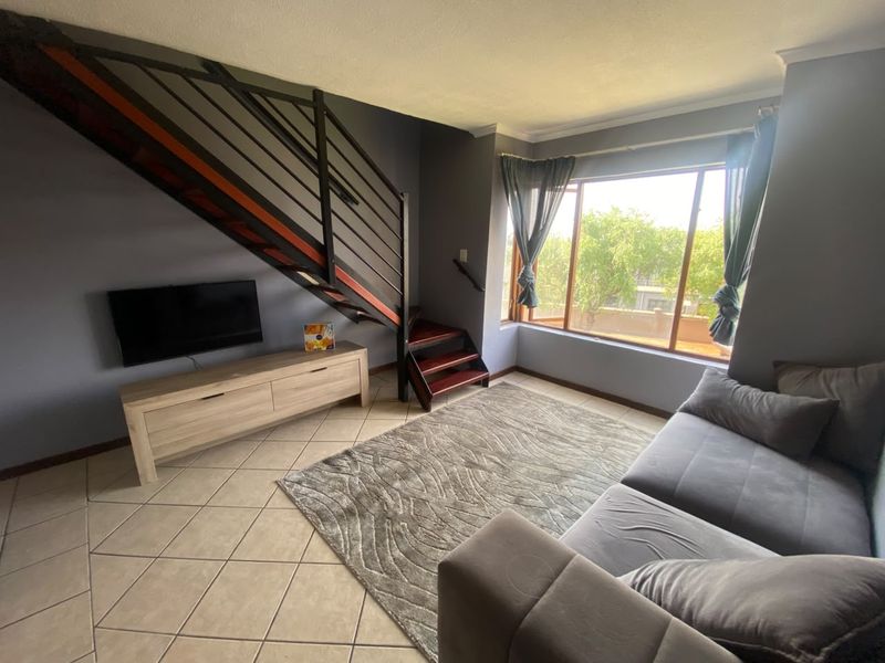 A living room featuring tiled flooring, a large window providing natural light, and an internal staircase with a metal balustrade.