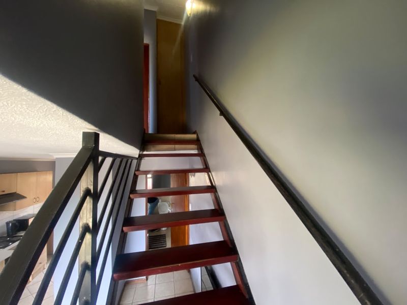 A staircase with wooden treads and a metal balustrade leading to an upper level, featuring tiled flooring and neutral wall finishes.