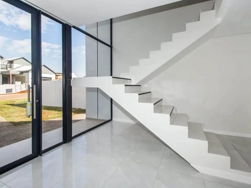 Modern entrance hall featuring a sleek white staircase, large glass sliding doors, and polished tiled flooring, offering a bright and contemporary welcome.