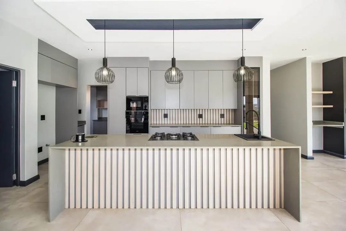Modern kitchen featuring a large island with gas hob, sleek grey cabinetry, integrated appliances, and stylish slatted timber detailing under a recessed ceiling.