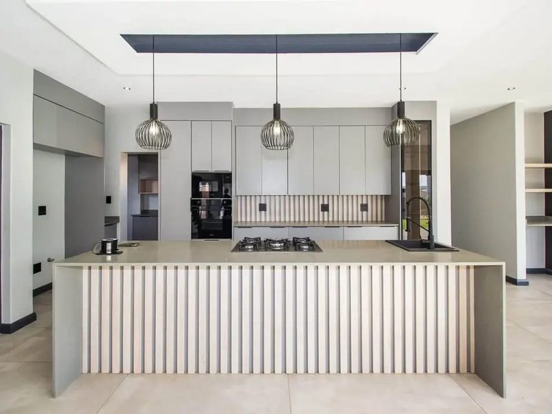 Modern kitchen featuring a large island with gas hob, sleek grey cabinetry, integrated appliances, and stylish slatted timber detailing under a recessed ceiling.