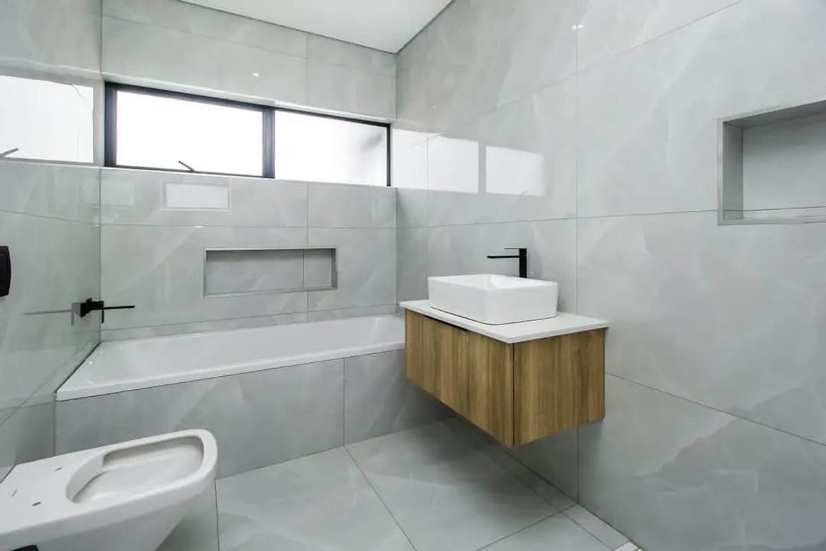 Modern bathroom featuring a wall-mounted vanity, vessel sink, built-in bathtub, and wall-hung toilet, finished with sleek large-format grey tiles and recessed storage niches.