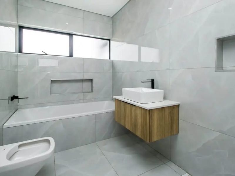 Modern bathroom featuring a wall-mounted vanity, vessel sink, built-in bathtub, and wall-hung toilet, finished with sleek large-format grey tiles and recessed storage niches.