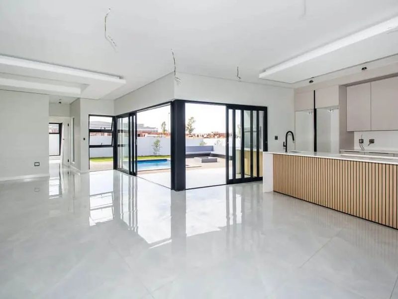 Spacious open-plan living and kitchen area featuring modern cabinetry, large sliding glass doors opening to a pool area, and high-gloss tiled flooring.