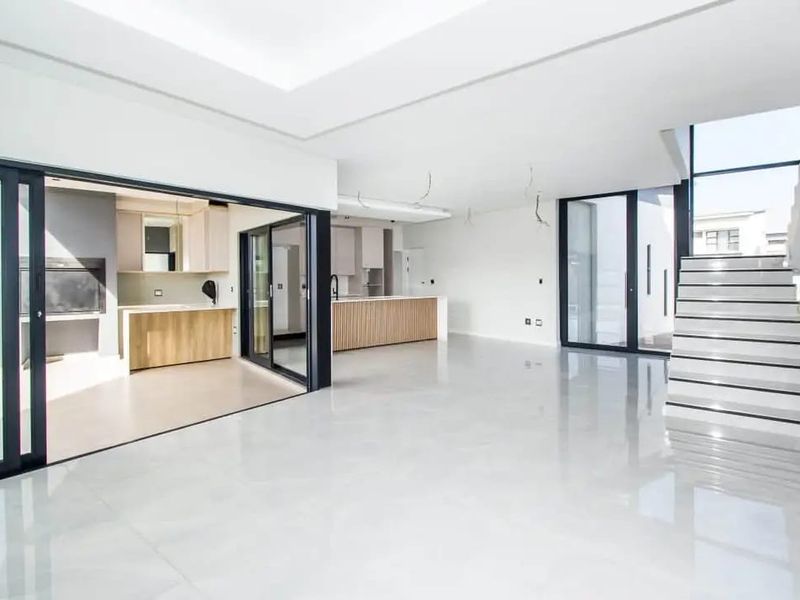 Spacious open-plan living and kitchen area featuring modern finishes, large sliding glass doors, and a sleek staircase in a contemporary apartment setting.
