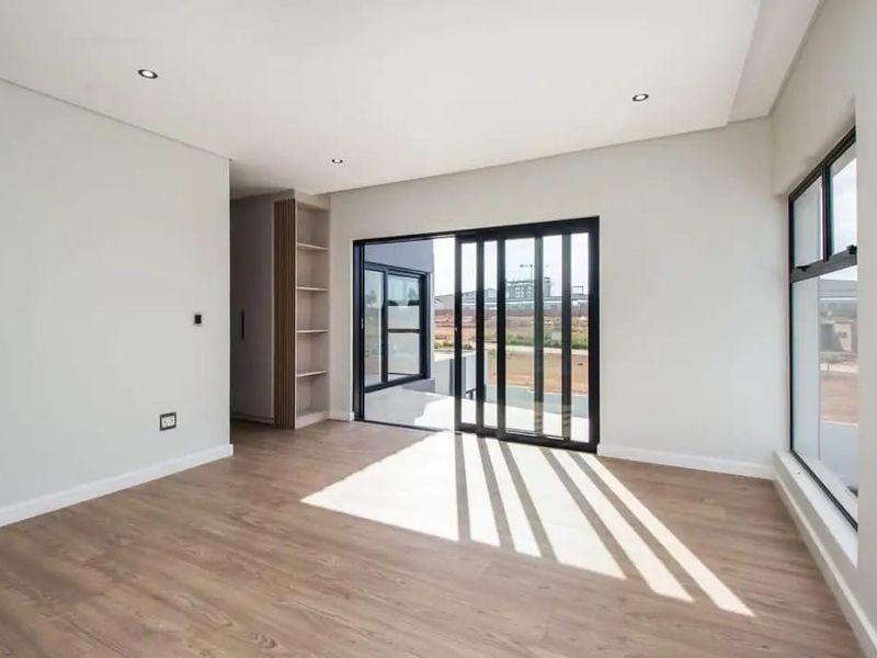 A bright, modern, and empty living area featuring laminate flooring, recessed lighting, built-in shelving, and large sliding glass doors leading to an outdoor space.