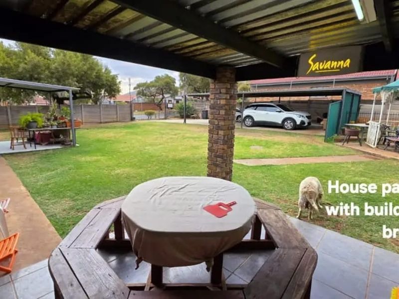 A covered outdoor patio area featuring brick pillars and tiled flooring, overlooking a spacious garden with additional outdoor structures.