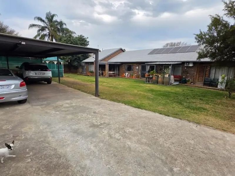 Rear view of the farm property featuring a spacious lawn, a covered carport, and solar panels installed on the tiled roof.
