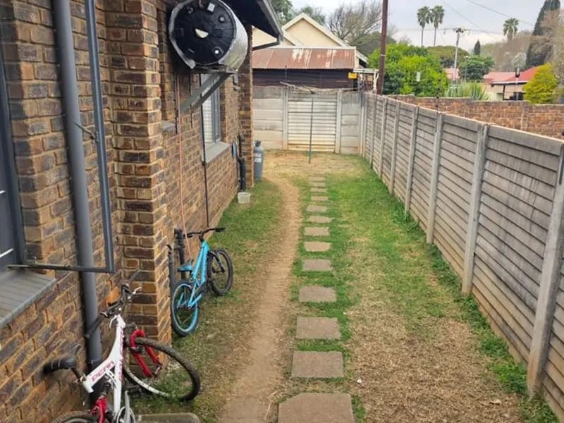 A side yard area featuring a face brick exterior wall, solar geyser, precast concrete boundary fencing, and a stone pathway leading to the rear garden.