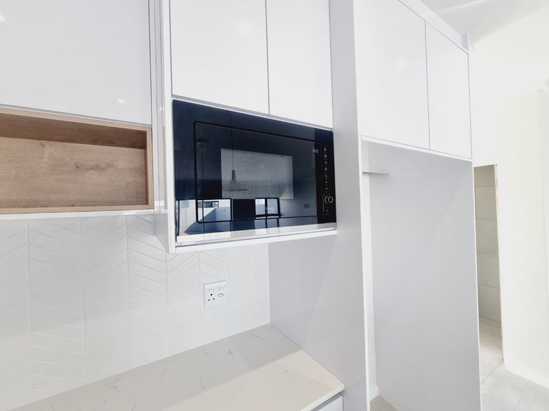 Modern kitchen area featuring white cabinetry, a built-in microwave, stone countertops, and a stylish herringbone tile backsplash.