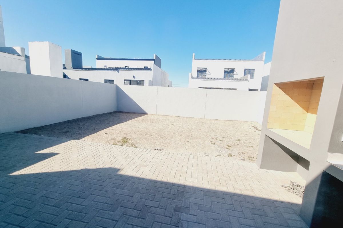 A private rear courtyard featuring a paved patio area and a built-in braai, enclosed by high boundary walls.
