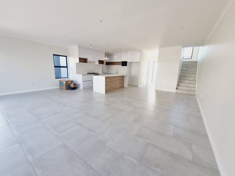 Spacious open-plan living area featuring a modern kitchen with a central island, tiled flooring, and a staircase leading to the upper level.