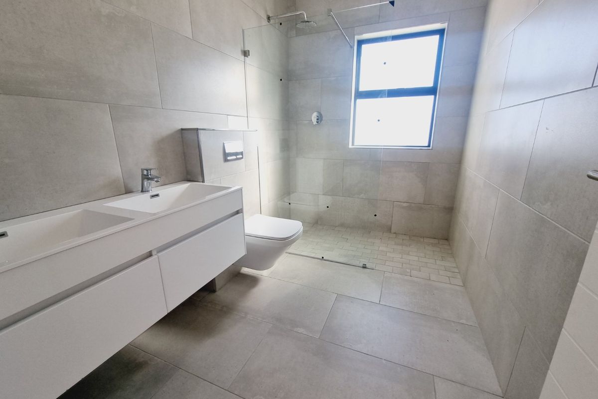 Modern bathroom featuring a wall-mounted double vanity, wall-hung toilet with concealed cistern, and a spacious walk-in shower with glass screen and neutral tiling.