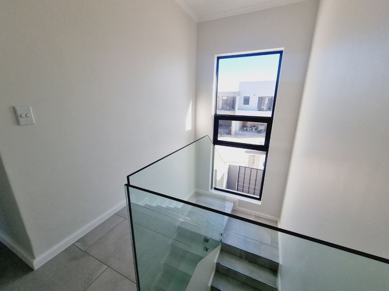 Modern staircase area featuring a sleek glass balustrade, large window providing natural light, and neutral tiled flooring in a contemporary home.