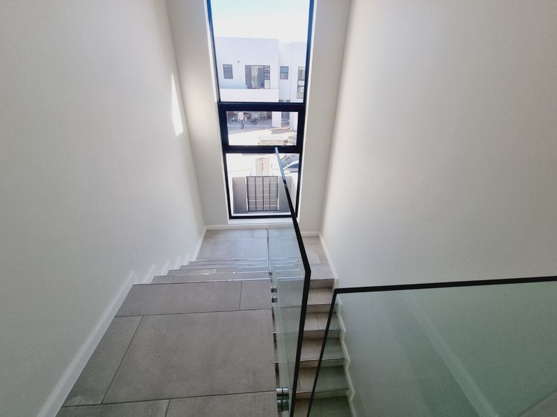 Modern staircase featuring large windows for natural light, glass balustrades, and clean tiled flooring in a contemporary home.