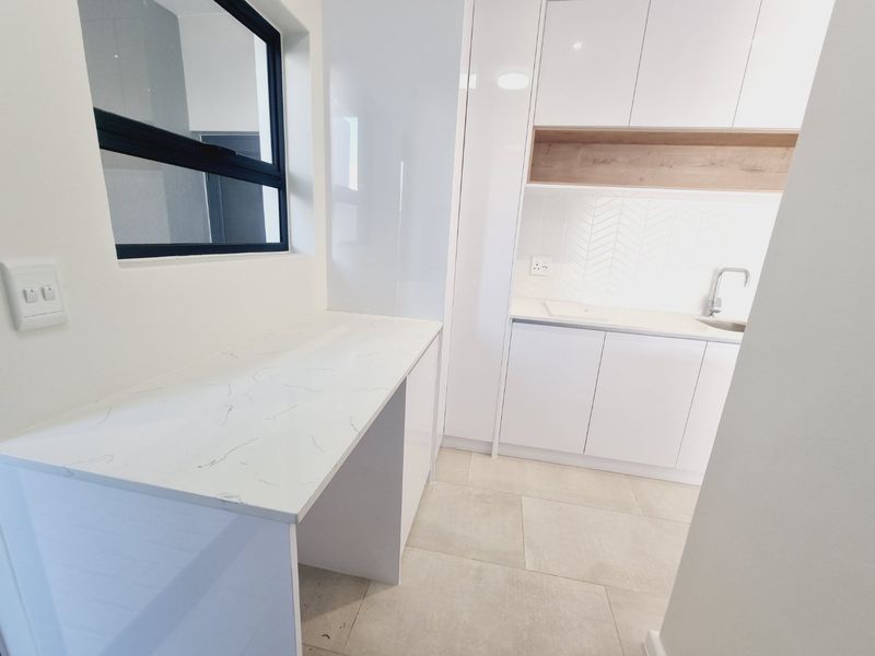 A modern, clean scullery featuring white cabinetry, marble-look quartz countertops, a herringbone tile backsplash, and a stainless steel sink.
