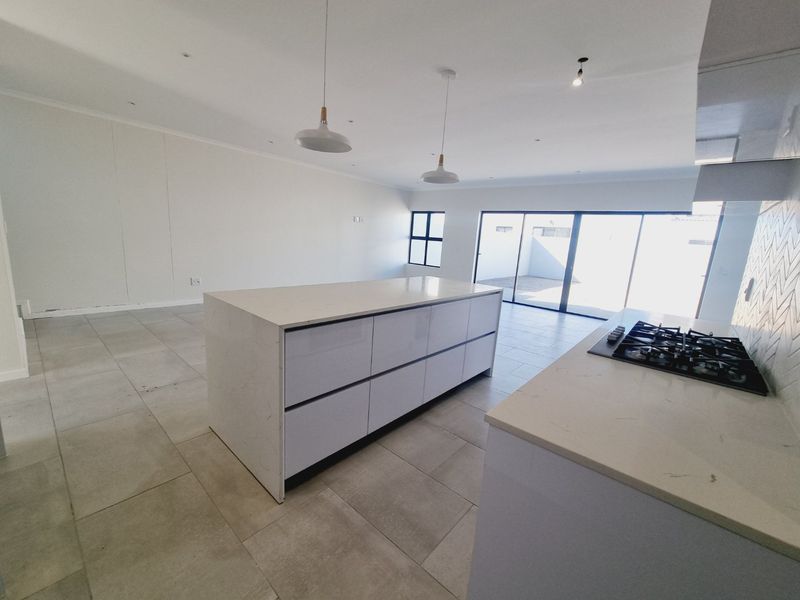 Modern open-plan kitchen and living area featuring a large central island, stone countertops, gas hob, and large sliding doors leading to the rear patio.