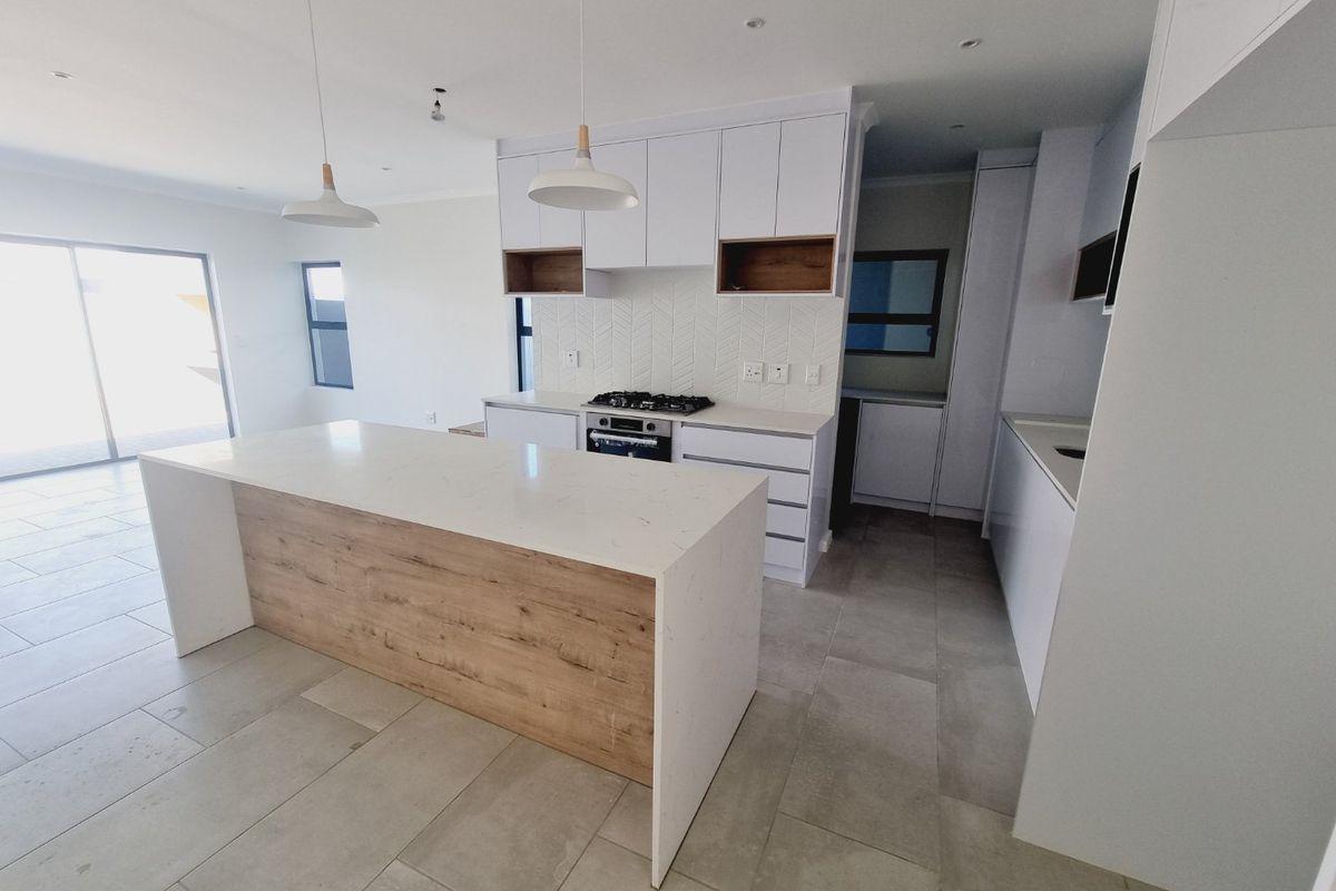 Modern open-plan kitchen featuring a central island with quartz countertops, gas hob, built-in oven, herringbone backsplash, and sleek white cabinetry with wood accents.