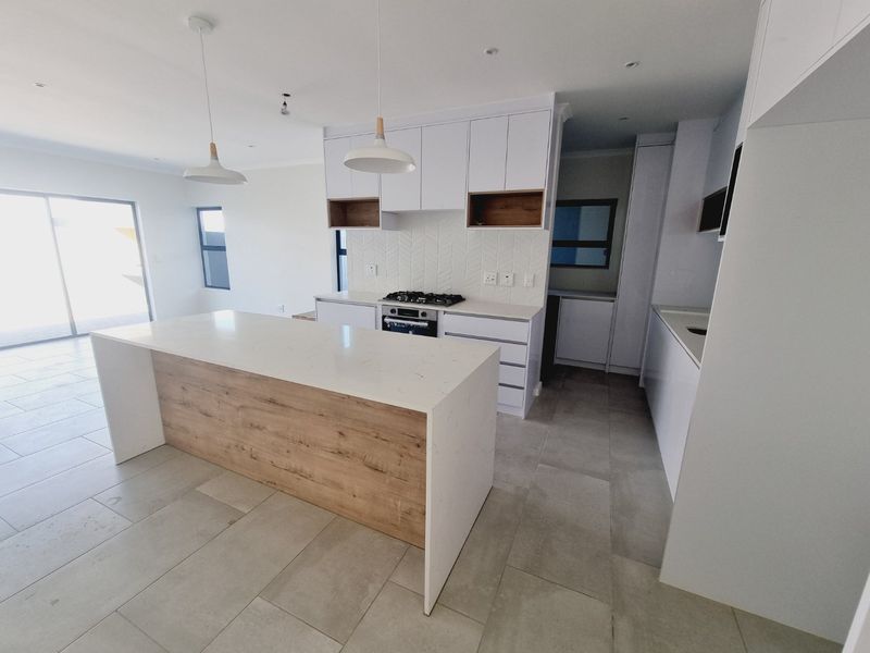 Modern open-plan kitchen featuring a central island with quartz countertops, gas hob, built-in oven, herringbone backsplash, and sleek white cabinetry with wood accents.