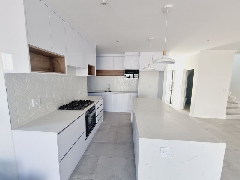Modern kitchen featuring white cabinetry, stone countertops, a central island, gas hob, and stylish herringbone tile backsplash in a bright, open-plan layout.
