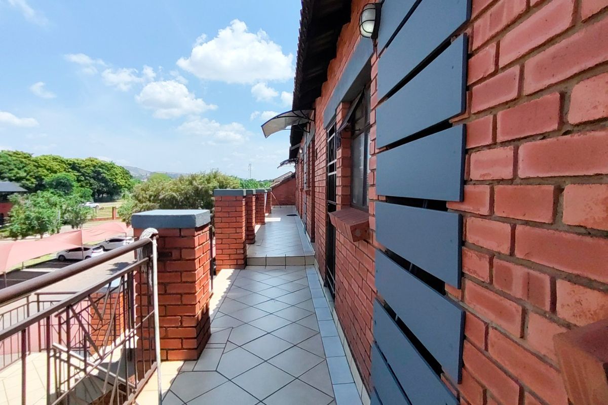A spacious, tiled balcony featuring exposed brickwork, metal railings, and an exterior wall light, offering an open outdoor area for the apartment.