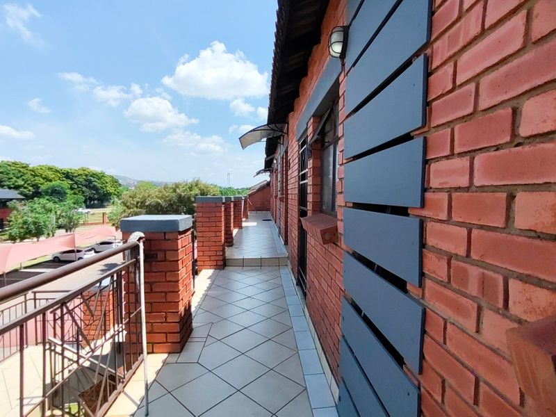 A spacious, tiled balcony featuring exposed brickwork, metal railings, and an exterior wall light, offering an open outdoor area for the apartment.