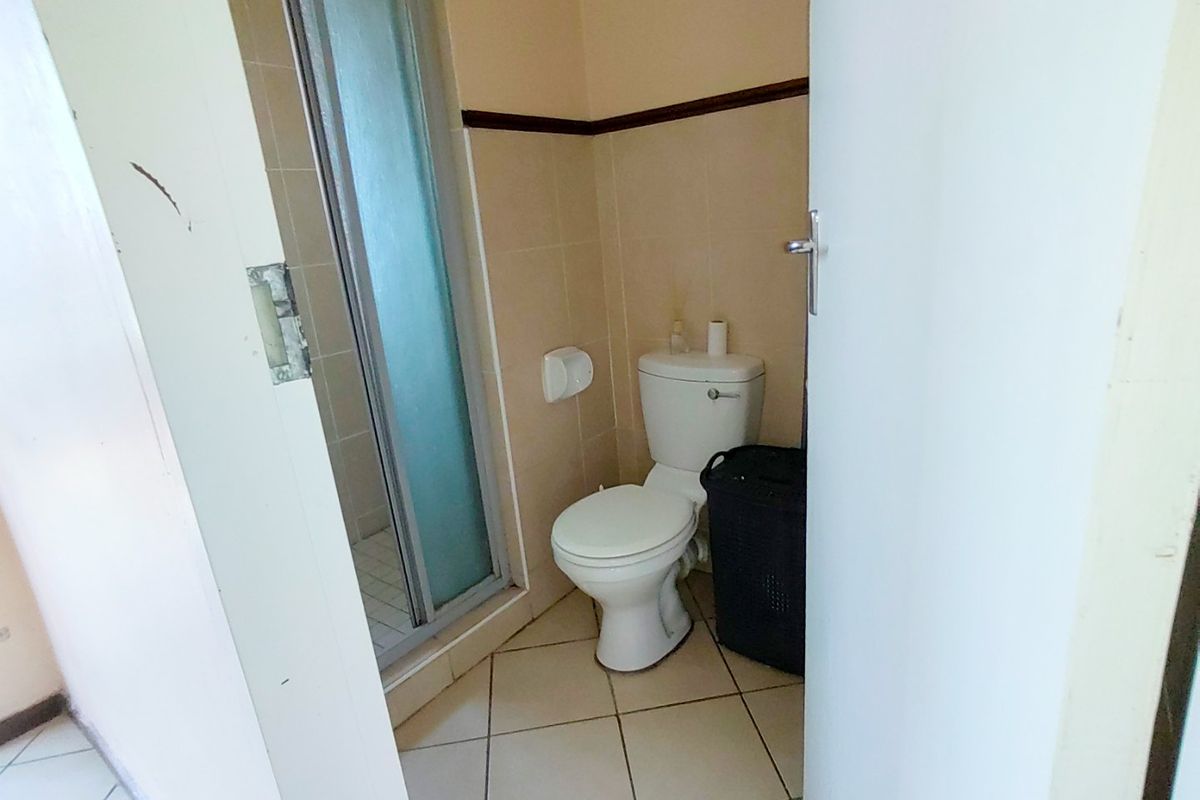 A compact bathroom featuring a shower enclosure and toilet with neutral wall and floor tiling, requiring some cosmetic updates to improve its overall condition.
