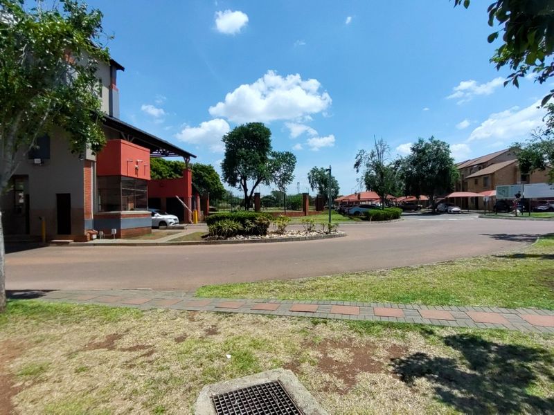 View of the apartment complex entrance featuring a security gatehouse, paved driveway, and well-maintained landscaped grounds.